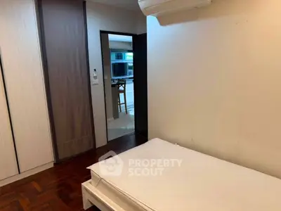 Cozy bedroom with wooden flooring and modern air conditioning unit, leading to a bright living area.