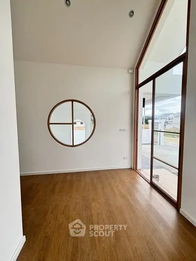 Modern interior with wooden flooring and large circular window, opening to a spacious deck.