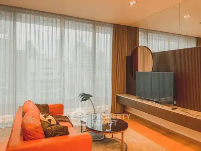 Modern living room with orange sofa, large windows, and stylish decor in urban apartment.