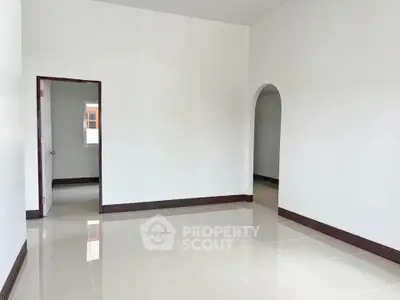 Spacious unfurnished room with glossy tiled floors and arched doorway, perfect for customization.