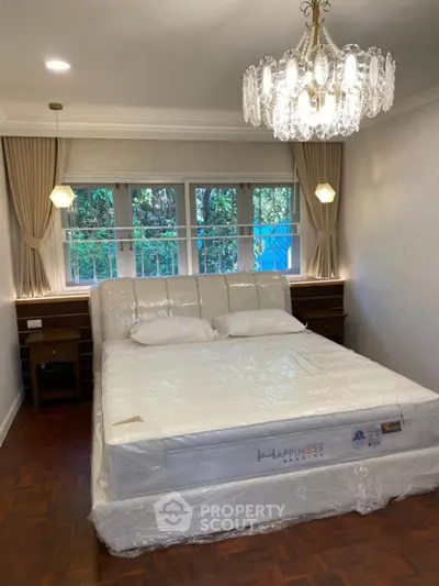 Luxurious bedroom with elegant chandelier and large windows overlooking greenery.