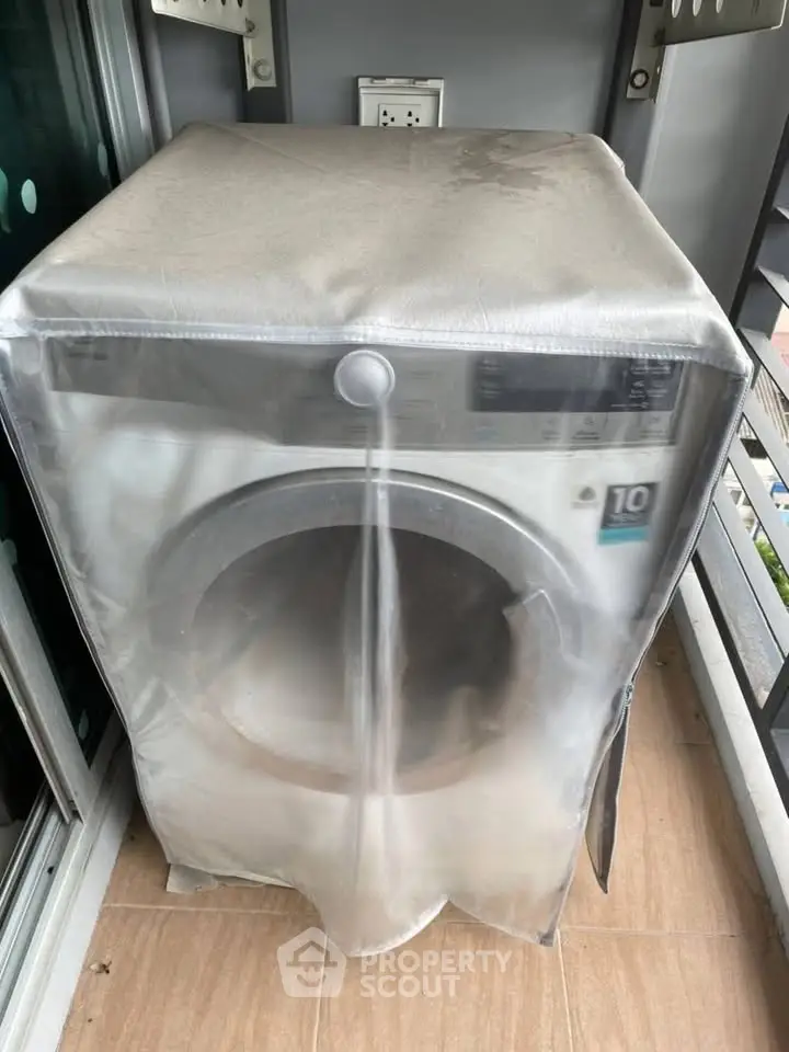 Covered washing machine on a balcony with modern railing and tiled floor.