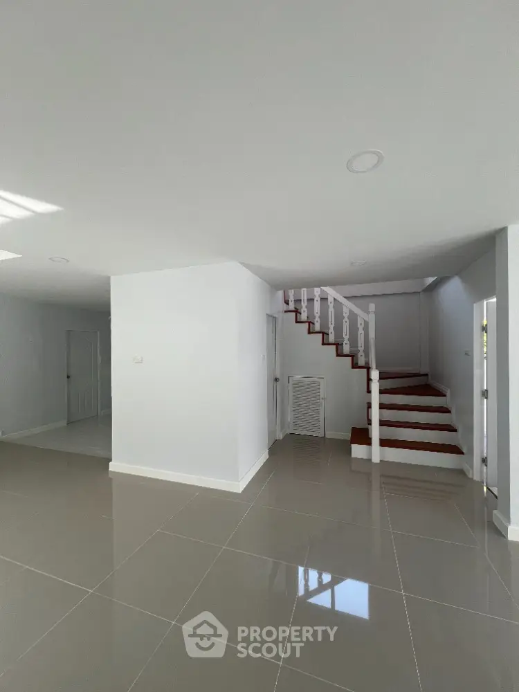 Spacious and bright open-plan living area with glossy tiled flooring and a striking red staircase leading to the upper level, perfect for modern living.