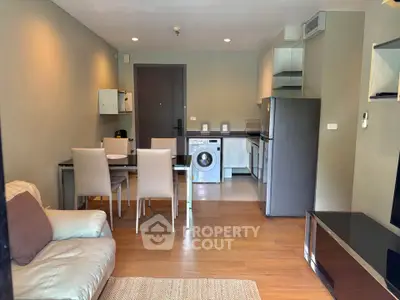 Modern open-plan living room with kitchen and dining area, featuring a washing machine and sleek furniture.