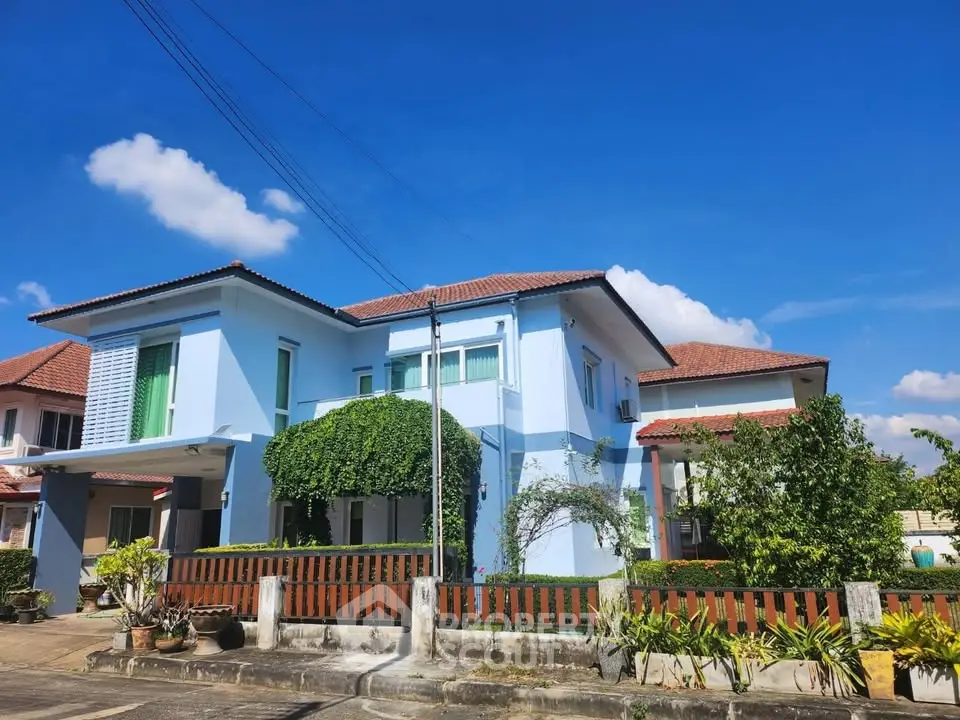 Charming blue two-story house with lush greenery and a sunny sky backdrop.
