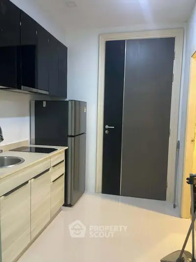 Modern kitchen with sleek cabinets and stainless steel fridge in compact layout.