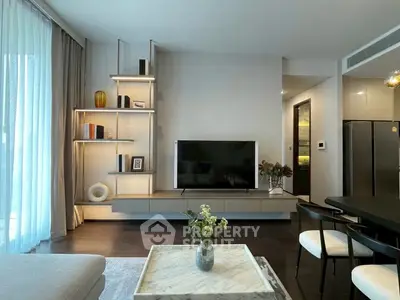 Modern living room with sleek furniture and large TV, featuring elegant shelving and natural light.