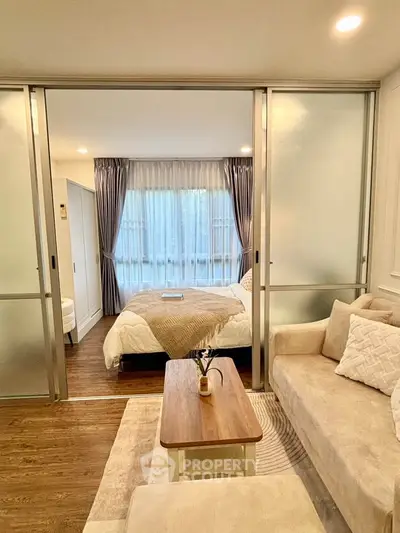 Modern studio apartment with cozy living area and bedroom separated by sliding glass doors.