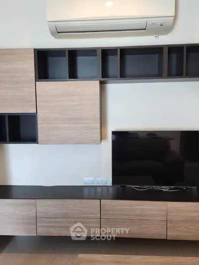 Modern living room with sleek wooden cabinetry and mounted TV under air conditioning unit.