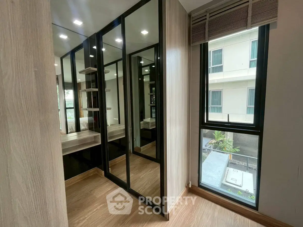 Modern walk-in closet with mirrored doors and natural light in a stylish apartment.