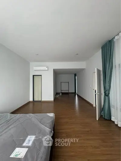 Spacious modern bedroom with wooden flooring and large windows in a minimalist apartment.