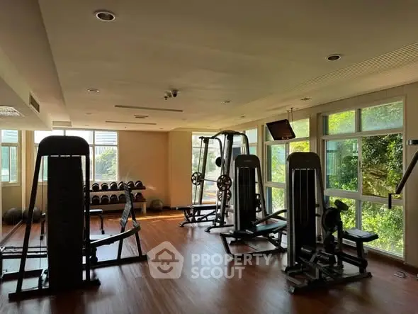 Spacious gym with modern equipment and large windows offering natural light.