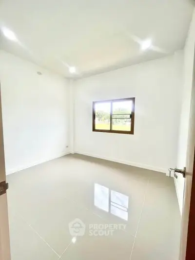 Spacious empty room with glossy tiled floor and large window, perfect for customization.