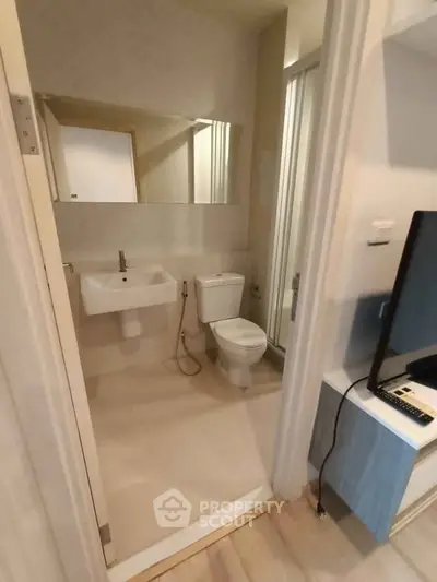 Modern bathroom with sleek fixtures and neutral tones, featuring a wall-mounted sink and shower area.