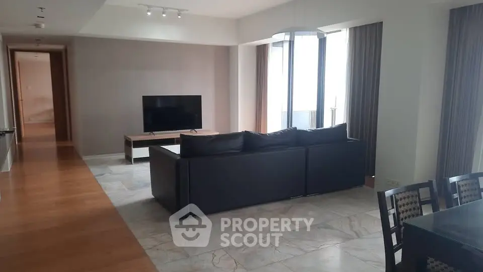 Spacious modern living room with sleek black sofa and large TV, perfect for relaxation.