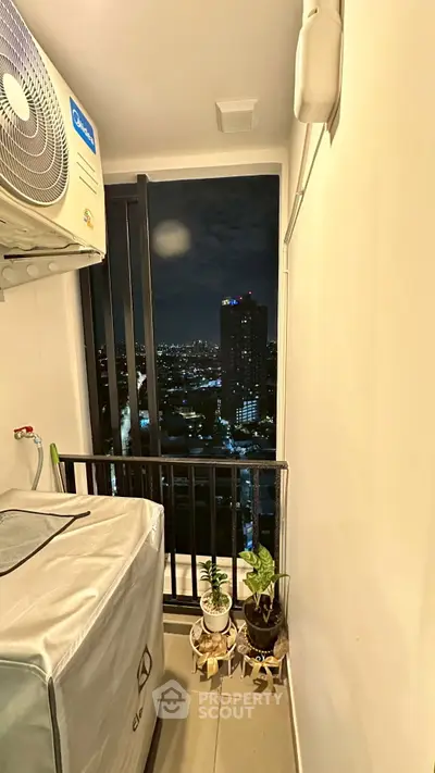 Compact balcony with city view, air conditioning unit, and potted plants at night.