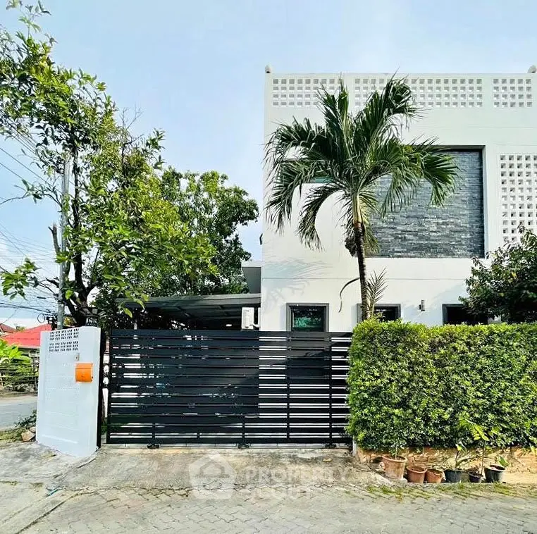 Modern minimalist house exterior with lush greenery and sleek black gate.