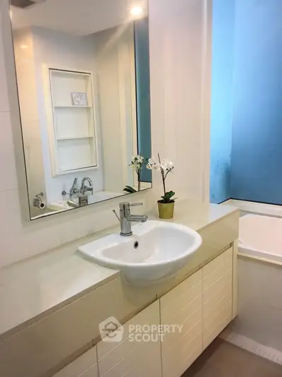 Modern bathroom with sleek sink and bathtub, elegant white cabinetry, and stylish mirror.