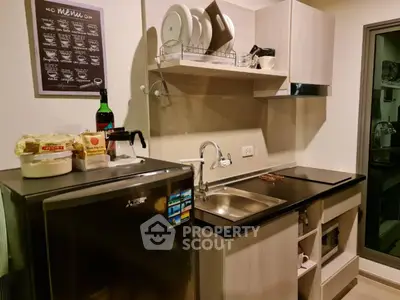 Modern compact kitchen with sleek cabinets and stainless steel sink, featuring a mini fridge and wall-mounted dish rack.