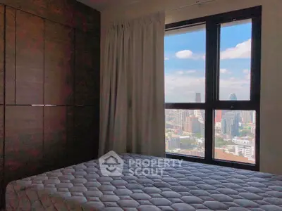 Cozy bedroom with city view through large window, featuring a comfortable bed and elegant curtains.