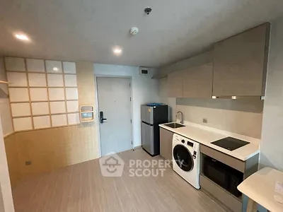 Modern kitchen with washing machine, fridge, and sleek cabinetry in compact apartment.