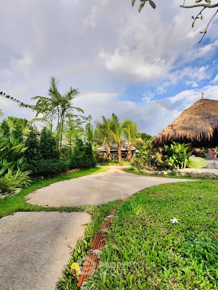 Tropical garden with lush greenery and thatched-roof huts under a vibrant sky.