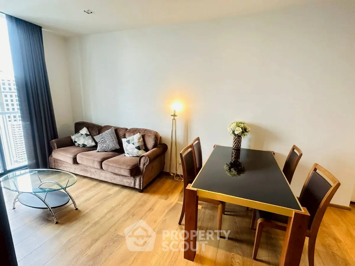 Modern living room with cozy sofa and elegant dining area, featuring wooden flooring and natural light.