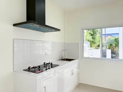Modern kitchen with gas stove and sleek white cabinetry, featuring a large window for natural light.