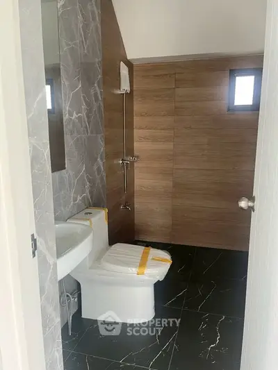 Modern bathroom with sleek marble and wood finishes, featuring a contemporary toilet and sink.