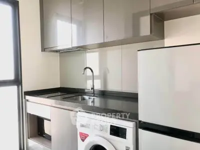 Modern kitchen with sleek cabinets, washing machine, and large fridge in a bright apartment.