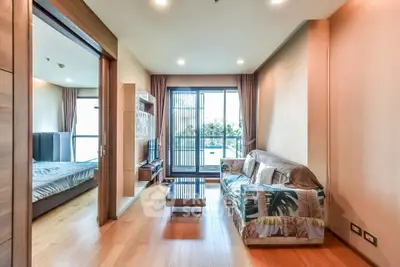Spacious living room with modern decor and natural light, adjacent to a cozy bedroom.