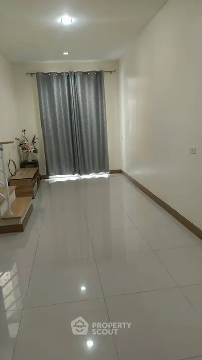 Spacious empty room with glossy tiled floor and large window with curtains.