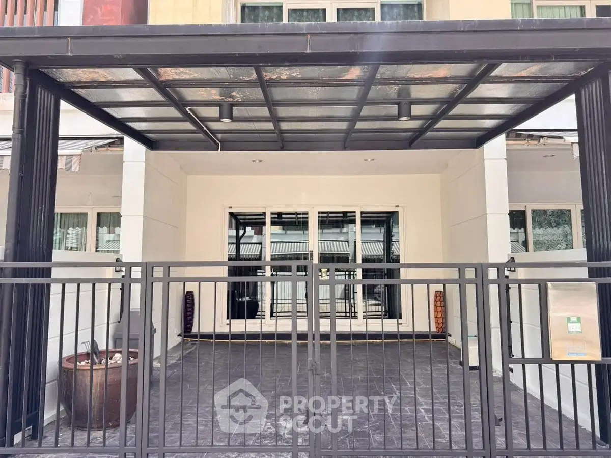 Modern house entrance with sleek metal gate and covered carport.