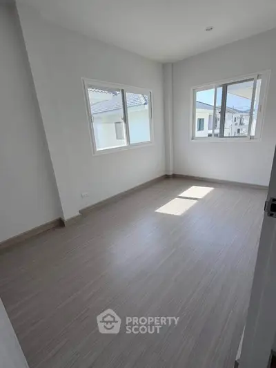Bright empty room with large windows and modern flooring in a new home.