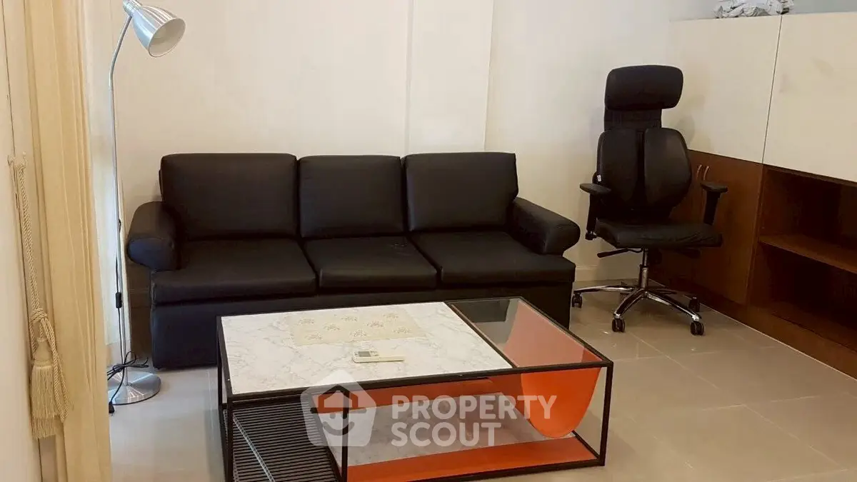 Modern living room with sleek black sofa and ergonomic chair, featuring a stylish glass coffee table.