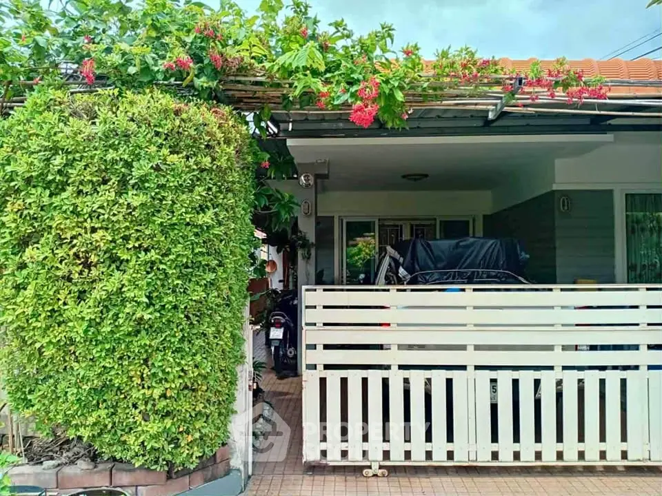 Charming house exterior with lush greenery and covered parking area.