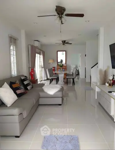 Spacious modern living room with elegant decor and dining area, featuring sleek furniture and ceiling fans.