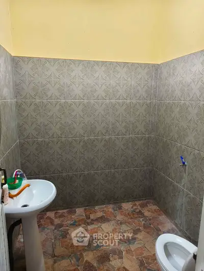 Spacious bathroom with tiled walls and floor, featuring a pedestal sink and toilet.