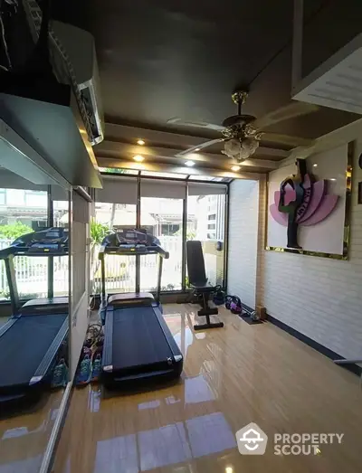 Modern home gym with treadmill and exercise equipment in bright room with large windows.