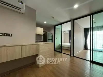 Modern apartment interior with open layout and wooden flooring, featuring a kitchen and glass partitioned bedroom.