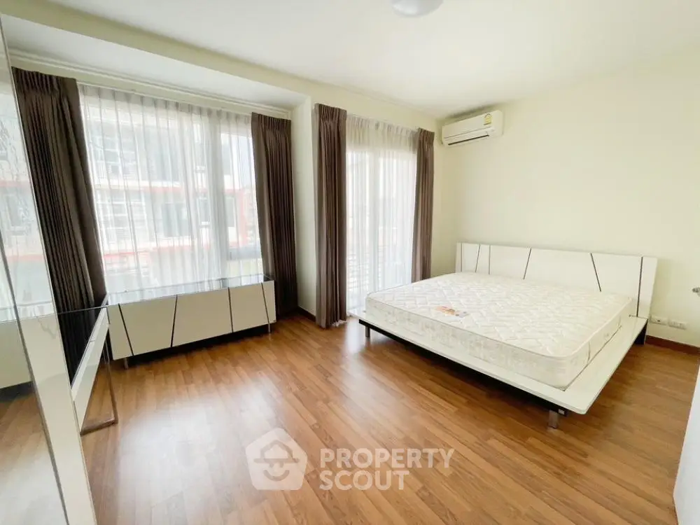 Spacious bedroom with large windows allowing ample natural light, hardwood flooring, and a modern air conditioning unit, perfect for comfortable living.
