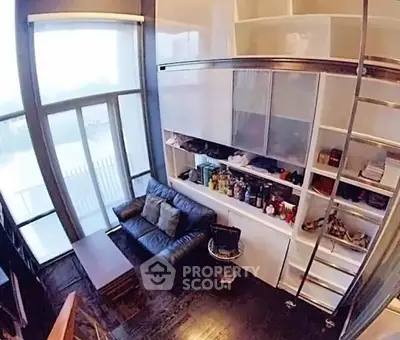 Modern loft-style living room with high ceilings and large windows, featuring a cozy sofa and built-in shelving.