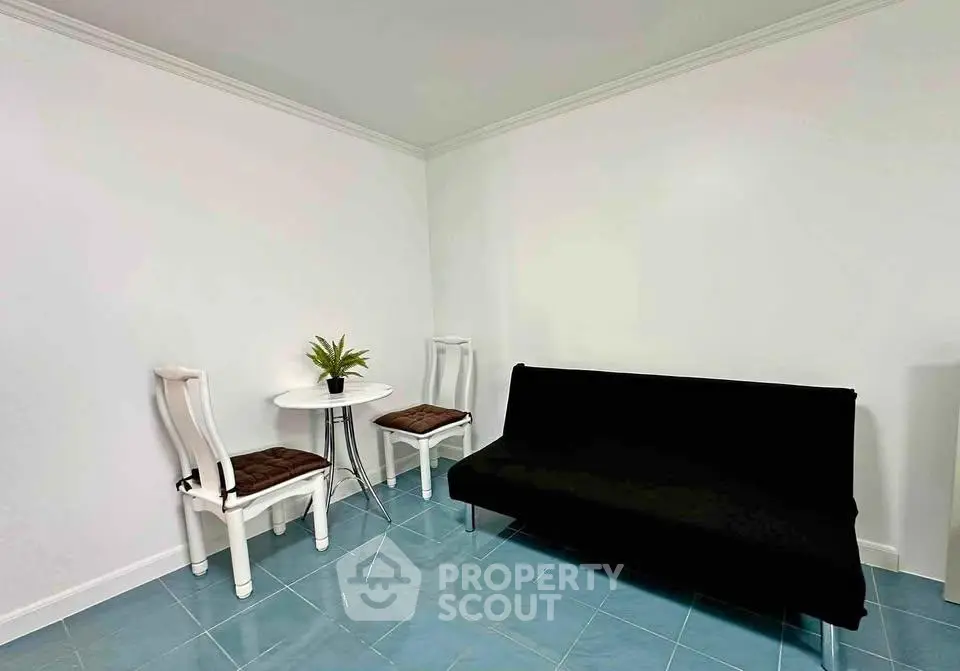Minimalist living room with black sofa, white chairs, and small table on blue tiled floor.