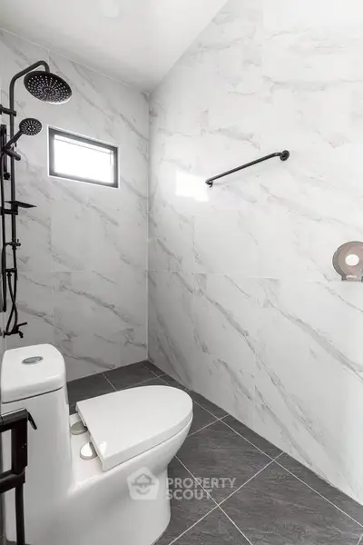 Modern bathroom with sleek fixtures and marble tiles, featuring a rainfall showerhead and contemporary toilet.