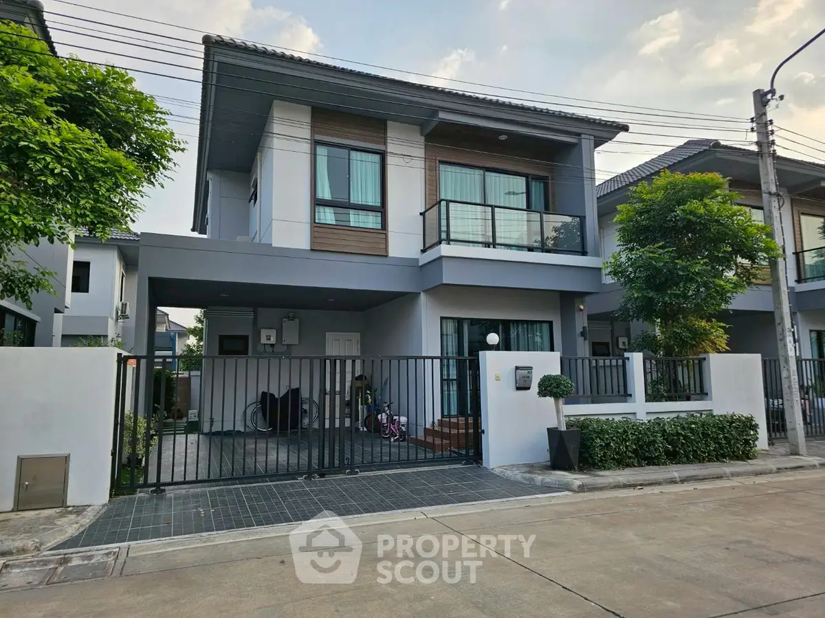 Modern two-story house with gated entrance and lush greenery