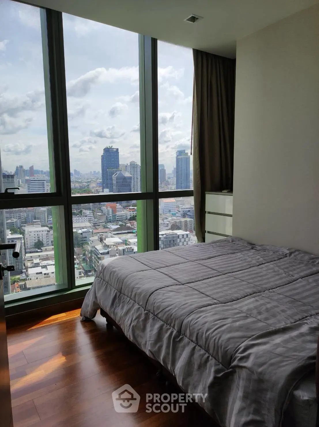 Modern bedroom with stunning city view through large windows, featuring sleek wooden flooring and cozy bedding.