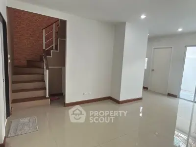 Spacious living area with gleaming tiled floors, modern white walls, and an elegant brick accent staircase leading to the upper level.