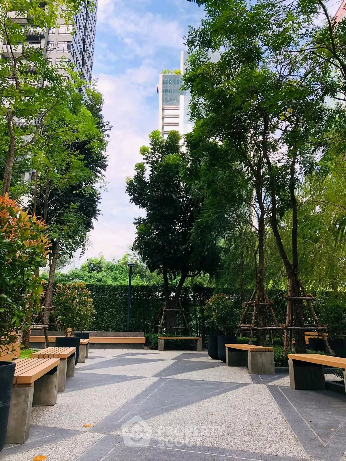 Tranquil garden area with benches and lush greenery in modern residential complex.