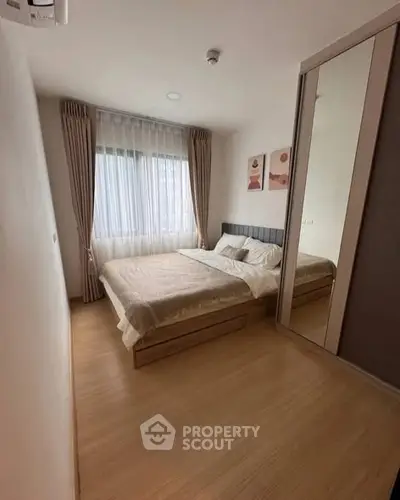 Cozy bedroom with large window and modern decor, featuring a comfortable bed and mirrored wardrobe.