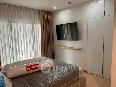 Modern bedroom with wall-mounted TV and large window, featuring sleek storage solutions and cozy ambiance.